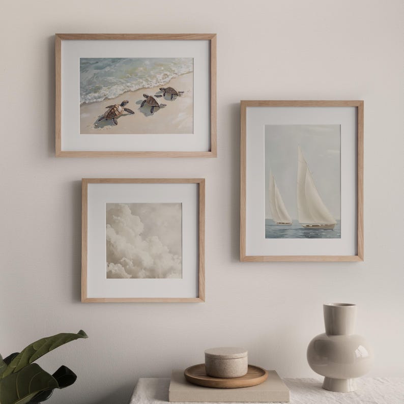 Op de afbeelding: Drie ingelijste prints op een witte muur. De print linksboven toont drie zeeschildpadden die in de oceaan zwemmen. De print rechtsboven toont twee zeilboten op het water. De print onderaan toont een bewolkte lucht.