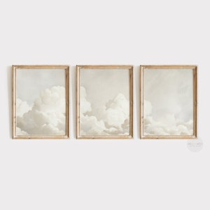 May include: Three framed prints of a painting depicting white clouds against a light grey sky. The frames are a light wood colour.