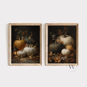 May include: Two framed art prints featuring a still life of pumpkins and autumn leaves. The pumpkins are in shades of orange, white, and green, with a dark background. One print includes a lantern. The frames are a light wood color.