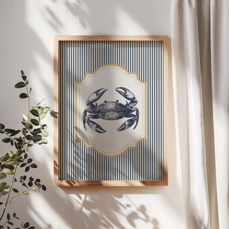 May include: A framed print with a navy blue crab illustration. The crab is set within a cream-colored, decorative shape, against a backdrop of navy and white vertical stripes. The frame is made of light-colored wood. The print is a nautical theme.