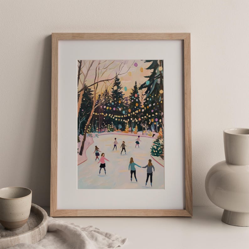 May include: A framed art print depicting an outdoor ice skating rink surrounded by evergreen trees and glowing string lights. Several figures are skating on the ice, which is set against a soft, muted sky. The frame is made of light-colored wood.