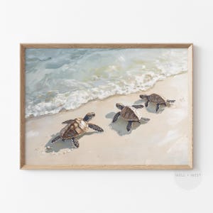 Op de afbeelding: Een ingelijste print van een schilderij met drie zeeschildpadden die in de oceaan zwemmen. De schildpadden zijn bruin en groen met lichtbruine schilden. De oceaan is lichtblauw met witte golven. Het zand is lichtbeige.