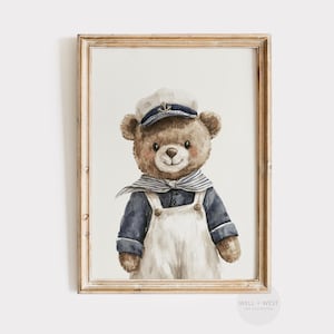 May include: Watercolor illustration of a teddy bear dressed as a sailor, wearing a navy blue and white striped sailor hat and scarf, and white overalls. The framed artwork has a gold-colored wooden frame.