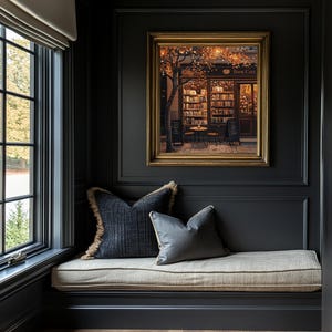 May include: A cozy reading nook with a framed painting of a "Book Cafe" with a gold frame. Two decorative pillows rest on a window seat with a neutral cushion. The walls are dark gray, and a window is visible.
