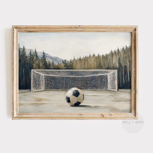 May include: Framed painting of a soccer ball on a field in front of a goal. The black and white ball sits on the field, with a net and trees in the background. The artwork is in a light-colored wooden frame.