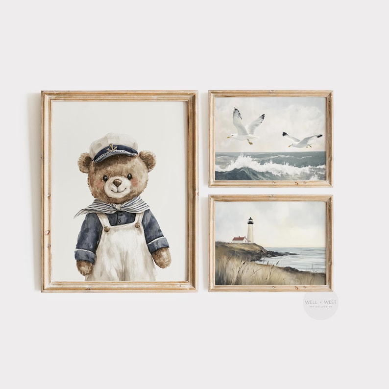 May include: A set of three framed wall art prints featuring a brown teddy bear wearing a navy blue shirt and white overalls with a sailor hat, a seascape with two white seagulls flying over ocean waves, and a lighthouse on a grassy coastal cliff.