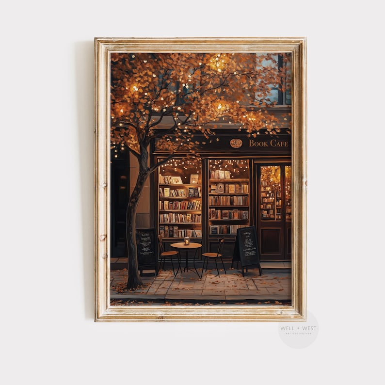 May include: A framed print of a cozy book cafe scene. The shop has a dark brown facade with large windows displaying shelves of books. A tree with orange leaves and string lights frames the entrance. Two small tables and chairs are set outside.