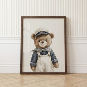 May include: A framed watercolor illustration of a brown teddy bear dressed as a sailor. The bear wears a white and navy blue sailor hat with a gold anchor emblem, a navy blue long-sleeved shirt, a striped neckerchief, and white overalls.