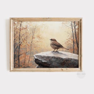 Puede incluir: Una pintura enmarcada de un pequeño pájaro marrón posado en una roca en un entorno boscoso. El fondo es una paleta suave y tenue de marrones, amarillos y verdes, creando una atmósfera pacífica y serena.