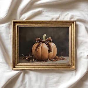 Puede incluir: Pintura enmarcada de una calabaza naranja con un lazo marrón y un tallo verde. La calabaza descansa sobre hojas caídas. El marco rectangular dorado añade un toque clásico.