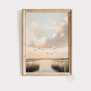 May include: A framed painting depicting a landscape with a pale blue sky, fluffy white clouds, and a tranquil body of water. The water is bordered by tall grasses and a few birds are flying in the sky.