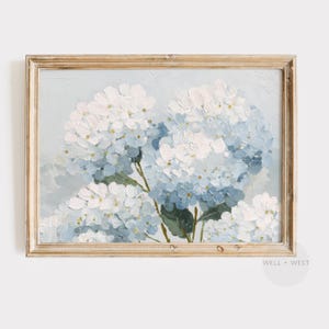 May include: A framed floral painting featuring blue and white hydrangeas. The artwork has a light blue background and is set in a light brown wooden frame. The painting has a textured, impressionistic style, with visible brushstrokes.