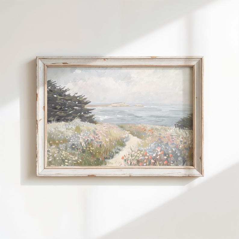 May include: A framed landscape painting depicting a coastal scene. The artwork features a path leading to the ocean, with colorful wildflowers and a tree on the left. The frame is white with a distressed finish, adding a vintage aesthetic.