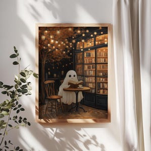 May include: A framed print depicts a friendly ghost reading a book at a cafe table. The scene is set at night, with warm string lights and a cozy bookstore in the background. The artwork has a whimsical, autumnal theme.