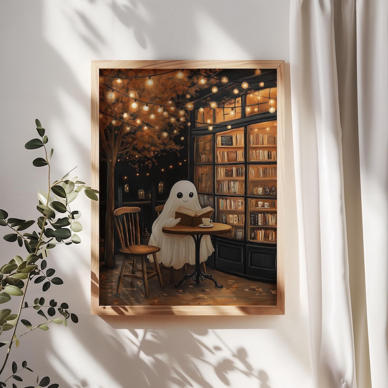 May include: A framed print depicts a friendly ghost reading a book at a cafe table. The scene is set at night, with warm string lights and a cozy bookstore in the background. The artwork has a whimsical, autumnal theme.