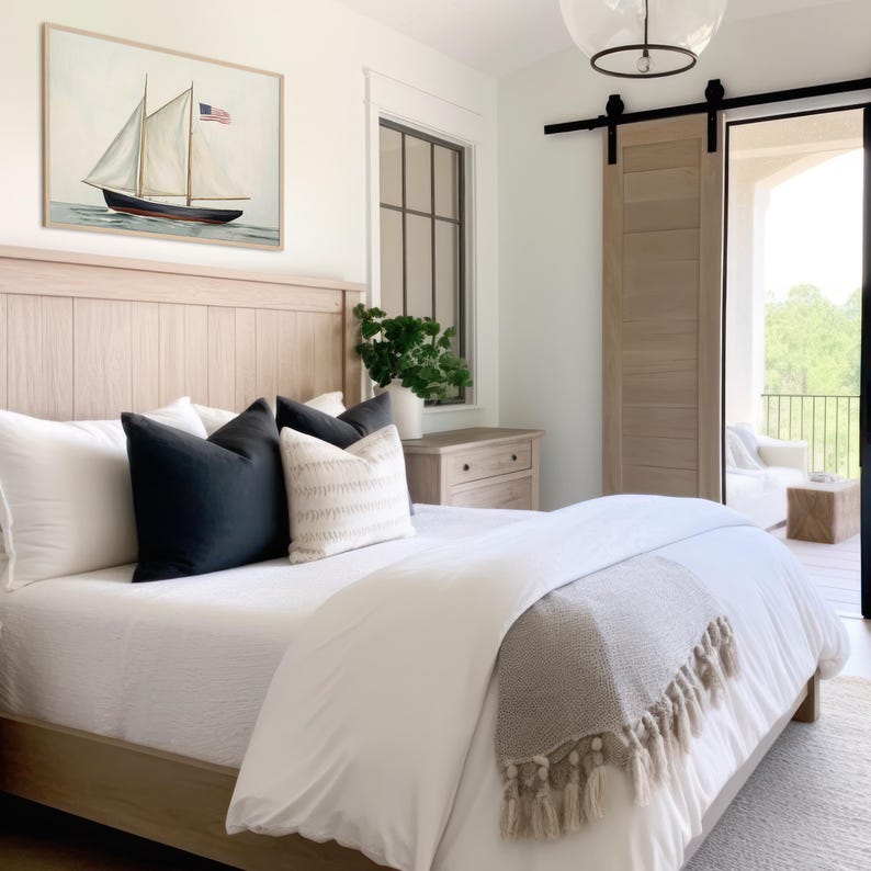 Peut inclure: Chambre avec lit en bois clair, literie blanche et coussins d&eacute;coratifs. Une peinture encadr&eacute;e d'un voilier avec un drapeau am&eacute;ricain est accroch&eacute;e au-dessus du lit. Une couverture grise &agrave; franges est drap&eacute;e au pied du lit.