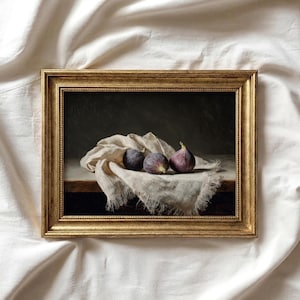 May include: A framed still life painting depicting three ripe figs on a linen cloth. The figs are a deep purple colour, with one having a green stem. The painting is in a gold-coloured frame.