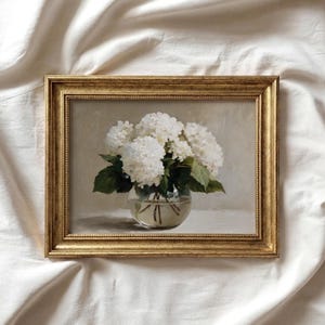 May include: A framed painting of white hydrangeas in a clear glass bowl. The painting has a gold-colored ornate frame. The background is a neutral color, and the flowers have green leaves.