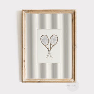 May include: Framed print featuring two crossed tennis rackets in a vintage style. The rackets are brown with white grips, set against a cream background. The frame is a distressed gold color, and the background has vertical gray and white stripes.