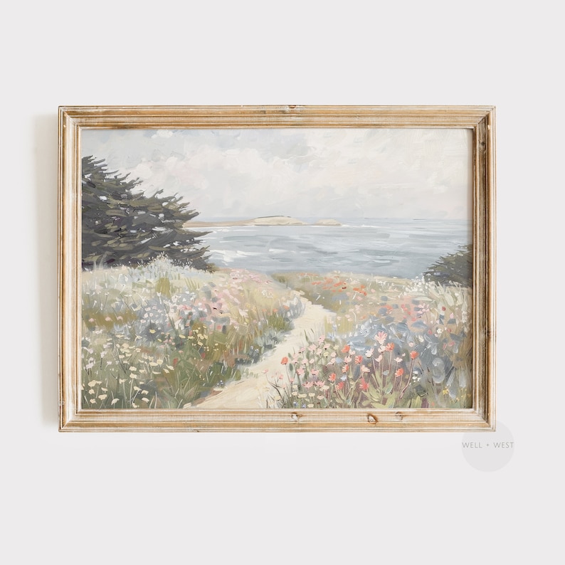 May include: A framed landscape painting depicts a coastal scene with a path leading to the ocean. The artwork features a muted color palette of blues, greens, and beige, with wildflowers and a tree in the foreground.