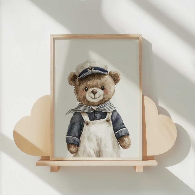 May include: A framed watercolor illustration of a brown teddy bear wearing a navy blue sailor shirt, white overalls, and a matching sailor cap with a gold anchor emblem. The bear has a striped neckerchief and is centered within a light wood frame.