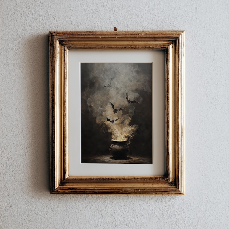 May include: A framed print showing a cauldron with smoke and bats. The artwork has a dark, atmospheric colour scheme and a gold frame. The cauldron is at the bottom, with smoke rising, and bats flying above.