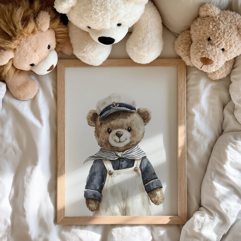 May include: A framed watercolor print featuring a brown teddy bear dressed as a sailor. The bear wears a white sailor cap with an anchor emblem, a navy blue shirt, a striped neckerchief, and white overalls. The frame is light-colored wood.