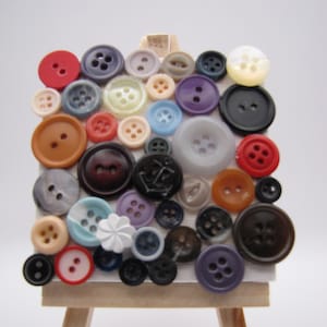 May include: A small wooden easel with a variety of colorful buttons arranged in a pattern. The buttons are different shapes, sizes, and materials, including plastic, metal, and fabric.