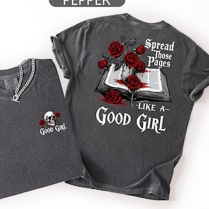 May include: A charcoal gray t-shirt featuring a small skull and rose graphic on the front chest. The back displays an open book with red roses and the text: Spread Those Pages LIKE A GOOD GIRL. The shirt has a crew neck and short sleeves.