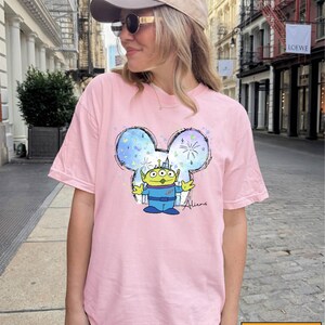 A woman wearing a pink t-shirt with a cartoon character printed on it, standing on a city street.
