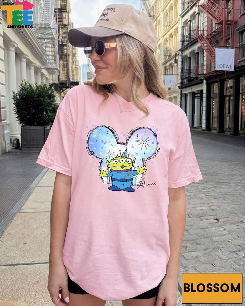 A woman wearing a pink t-shirt with a cartoon character printed on it, standing on a city street.