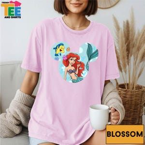 A woman wearing a pink t-shirt with a Disney character printed on it, sitting on a couch with a cup of coffee in front of her.