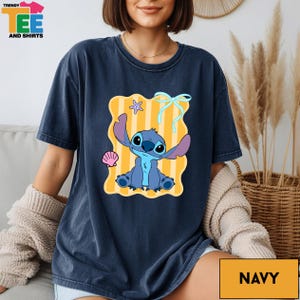 A woman wearing a navy blue t-shirt with a cartoon character printed on it, sitting on a couch.