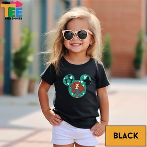 A young girl wearing a black t-shirt with a Disney character design and sunglasses, smiling at the camera.