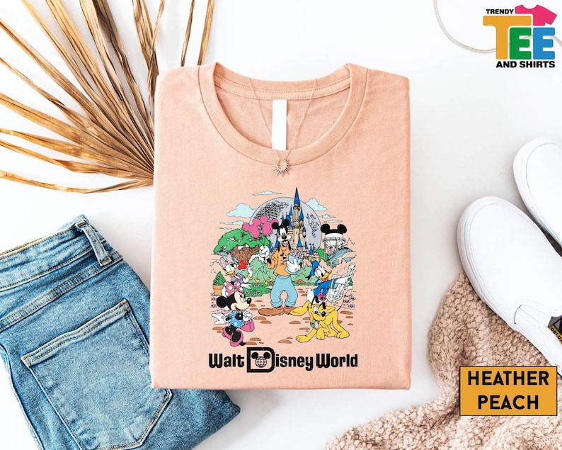 May include: A peach colored t-shirt with a graphic of Mickey Mouse and other Disney characters in front of Cinderella's Castle. The text "Walt Disney World" is printed below the graphic.