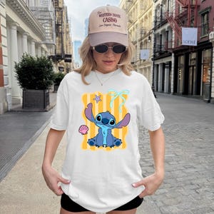 A woman wearing a white t-shirt with a cartoon character printed on it, standing on a city street.