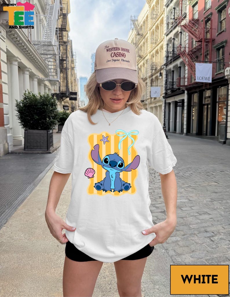 A woman wearing a white t-shirt with a cartoon character printed on it, standing on a city street.