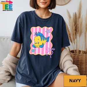 A woman wearing a navy blue t-shirt with a cartoon fish design and a pink and yellow striped background.