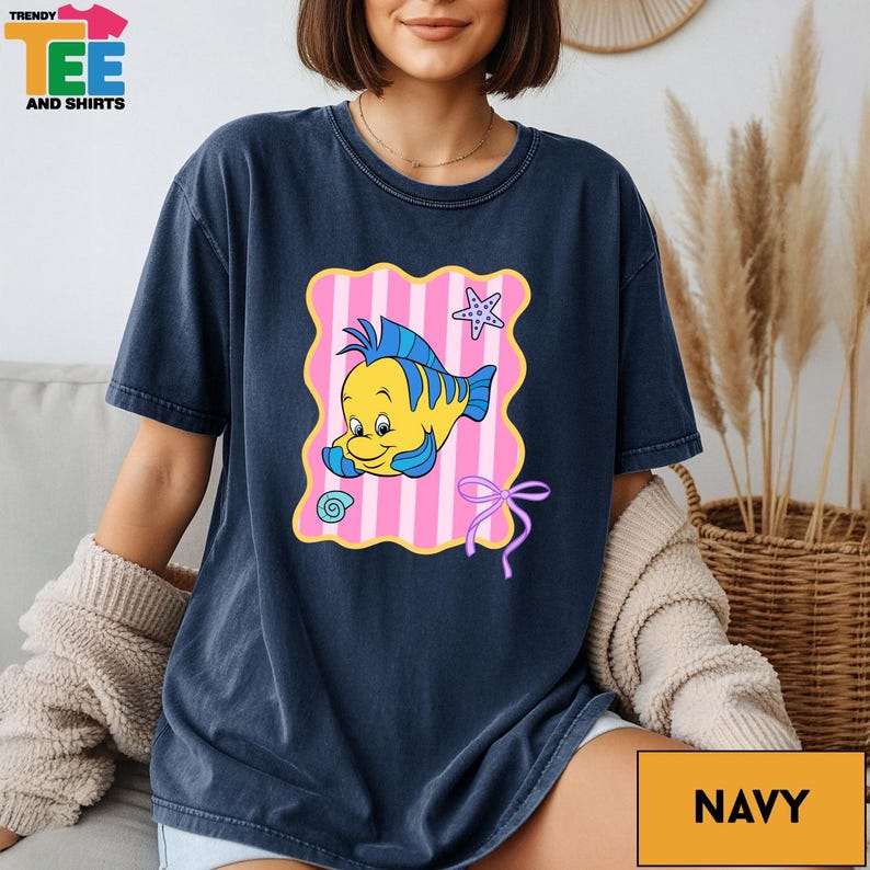 A woman wearing a navy blue t-shirt with a cartoon fish design and a pink and yellow striped background.