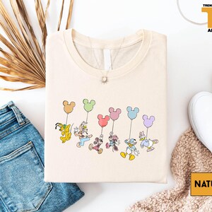 a casual outfit with a t-shirt featuring a group of Disney characters, including Mickey Mouse, Donald Duck, Goofy, and Minnie Mouse, along with a pair of jeans and white sneakers.