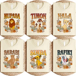 May include: Six cream-colored t-shirts featuring characters from The Lion King. Each shirt displays a character's name in a retro font, accompanied by a floral design and a character illustration. Characters include Mufasa, Timon, Nala, Sarabi, Simba, and Rafiki.