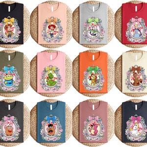 May include: A collection of t-shirts in various colors, each featuring a different cartoon character design. The designs are framed by a floral oval and a decorative bow. The shirts are displayed on a woven surface.