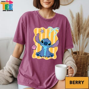A woman wearing a purple t-shirt with a cartoon character from the movie Lilo and Stitch, sitting on a couch with a cup of coffee in front of her.