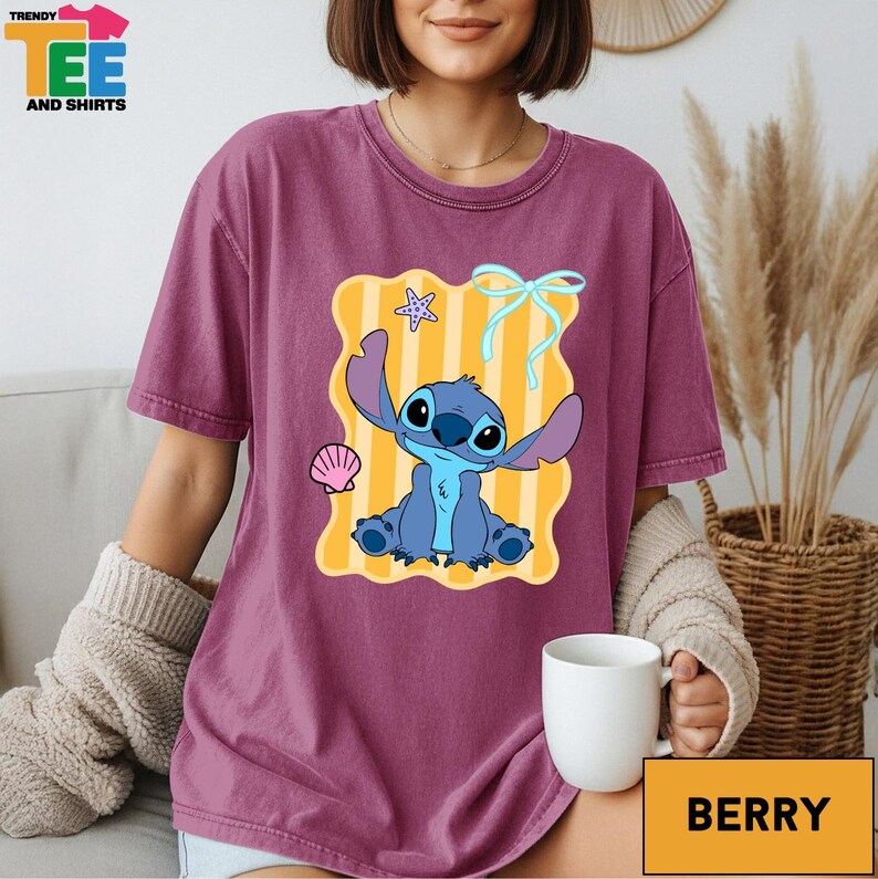 A woman wearing a purple t-shirt with a cartoon character from the movie Lilo and Stitch, sitting on a couch with a cup of coffee in front of her.