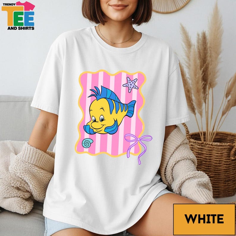 A woman wearing a white t-shirt with a cartoon fish design and a pink and white striped background.