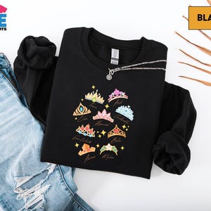 a black sweatshirt with a colorful crown design, a pair of blue jeans, and a black shirt with a chain.