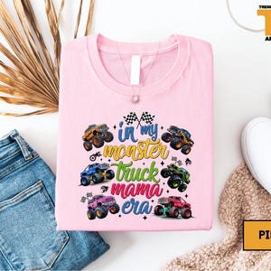 a pink t-shirt with a colorful graphic design of monster trucks, along with a pair of jeans and a pair of white sneakers.