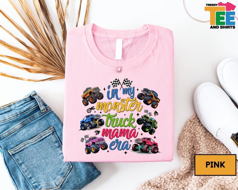 a pink t-shirt with a colorful graphic design of monster trucks, along with a pair of jeans and a pair of white sneakers.