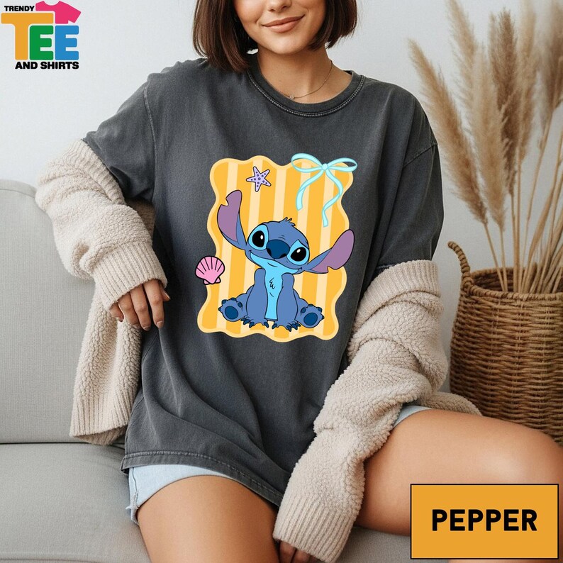 A woman wearing a gray t-shirt with a cartoon character printed on it, sitting on a couch.