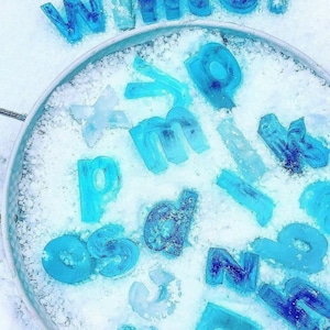 Peut inclure: Un plateau en métal rempli de neige et de lettres en plastique bleues qui épellent le mot "hiver".